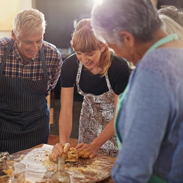 Three people, two adults and one younger woman, happily kneading dough together on a wooden table.