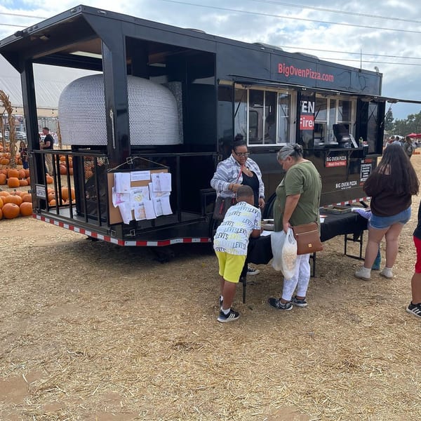 A Big Oven Pizza mobile truck with a wood-fired oven, serving customers at an outdoor event.