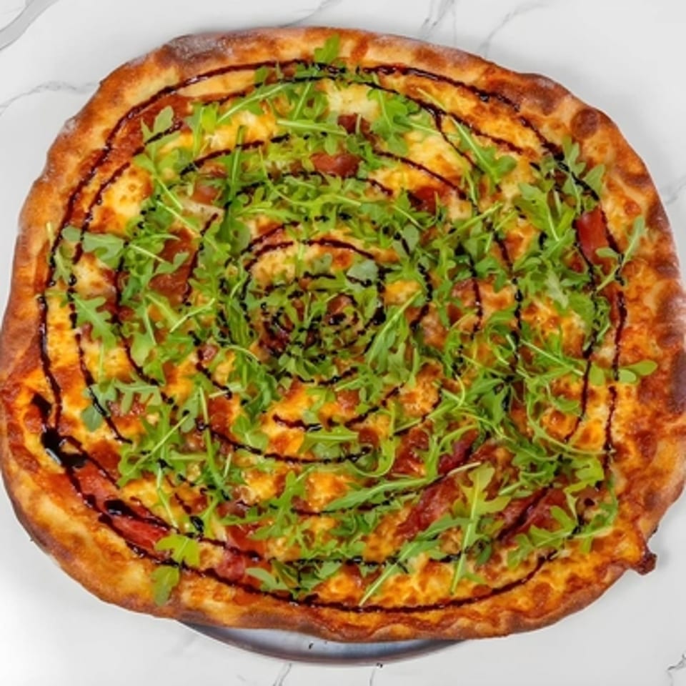 A Big Oven Pizza with arugula, pepperoni, and a balsamic glaze swirl on a white marble surface.