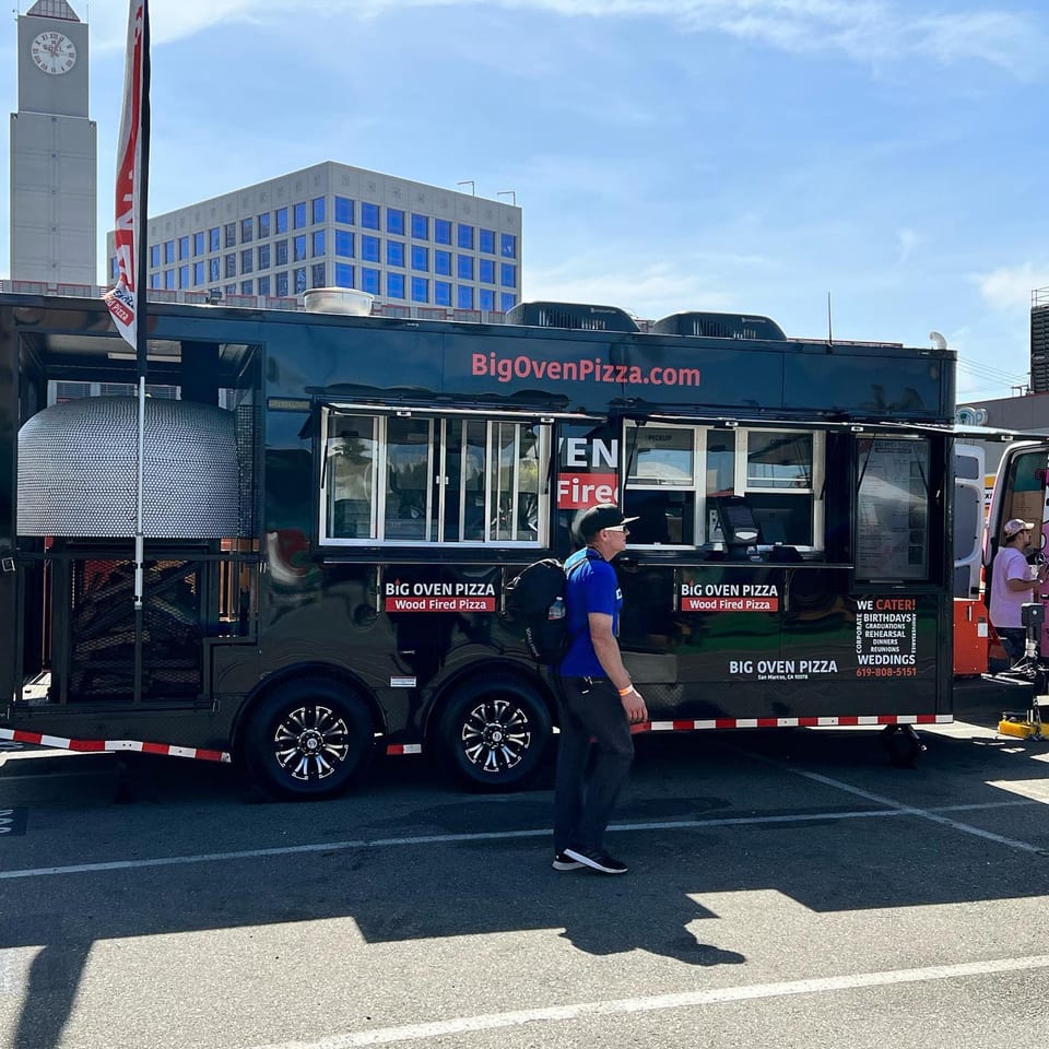 Big Oven Pizza mobile truck with a wood-fired oven, parked outdoors with people nearby.