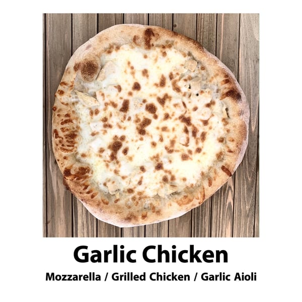 A round Garlic Chicken pizza with mozzarella, grilled chicken, and garlic aioli on a wooden surface.